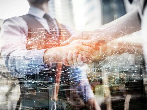 A semi-transport image of two businessmen shaking hands, a modern city skyline in the background.Dots  and lines overlay the scene, symbolising a digital connectivity between them. 