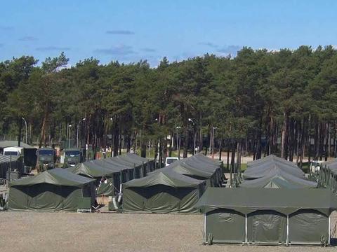 Military tent and container based infrastructure on sandy ground in front of a forest 