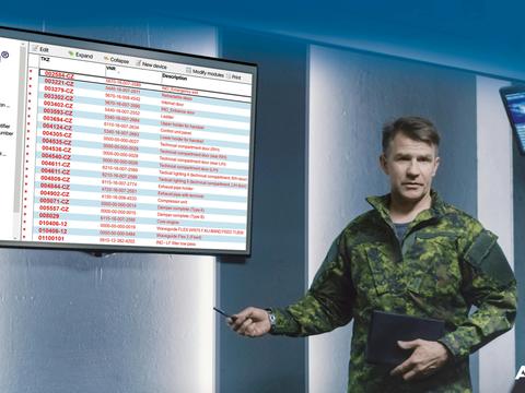 A Soldier in a modern operation centre standing next to a screen displaying a table of SMaC. Additional screens and soldiers working on computers are visible in the background.