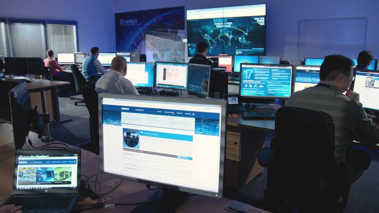 A group of people seated at computers in an indoor office environment at an IMINT and GEOINT Centre. 